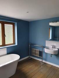 Picture of chic modern bathrrom with a free standing bath, and towel radiator on show. The walls have been painted in a matt blue giving. The floorboards have also been varnished giving the room a vintage look. 