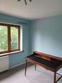 Picture of a domestic bedroom painted in matt emulsion in a deep turquoise. The room looks out to the rear and the daylight is shining through the window. There is also an old wooden piano in the room