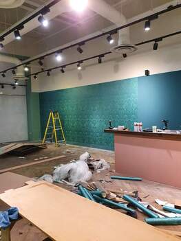Picture showing a retail shop in the middle of being redecorated. There is a shop counter is in view and behind it, the walls are being covered with teal designer wallpaper and paint