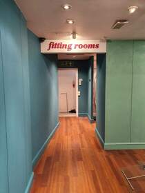 Picture showing the entrance to the fitting rooms in a modern retail shop refurbishment. Wall panels are painted in turquoise and light blue. Spotlights adorn the suspended ceiling, which is painted in white emulsion.