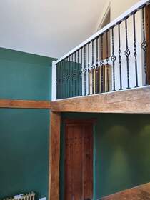 Picture of a mezzanine floor within a house. The floor is supported by exposed original timber beams. The guard rails are painted in black gloss with white handrails and the wall is painted in teal emulsion.