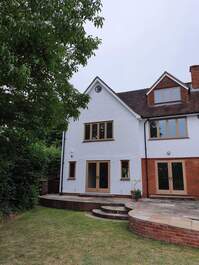 Picture of the rear of a house that is part render and part brickwork. The external render has been painted in a white colour and the external windows are brown timber.