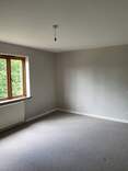 Picture of a bedroom with a light grey matte emulsion paint on the walls and white gloss skirting boards. The window in the room is treated timber with a natural finish. Natural daylight is shining into the room