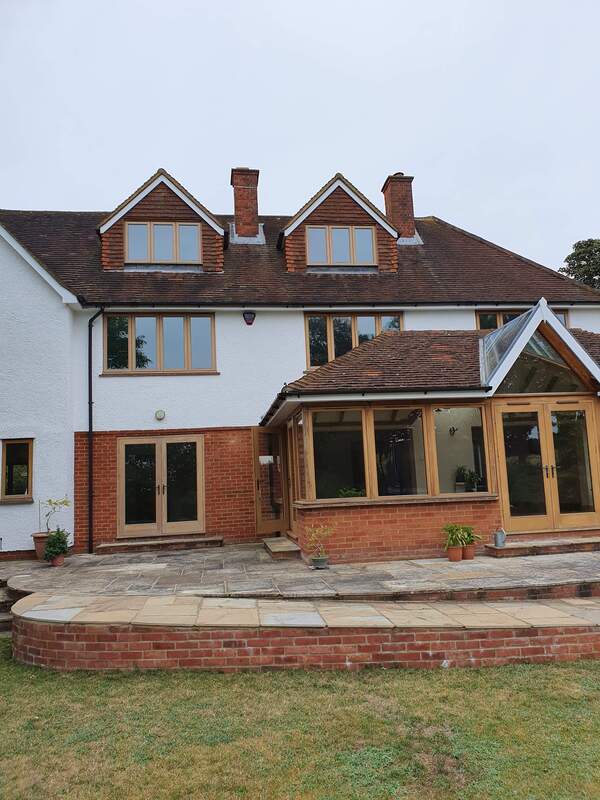 Picture the exterior of a house taken from the rear garden. The proprty is a mixture of brickwork at the bottom an white painted render at the top. It has timber windows and a large paved patio area outside the house. 