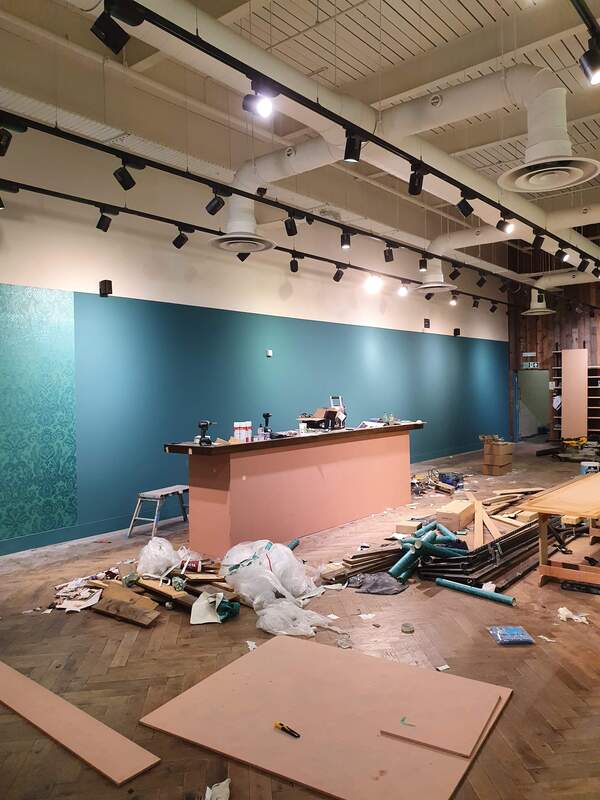 Picture of the inside a retail store that is being redecorated with designer wallpaper and turquoise paint. 